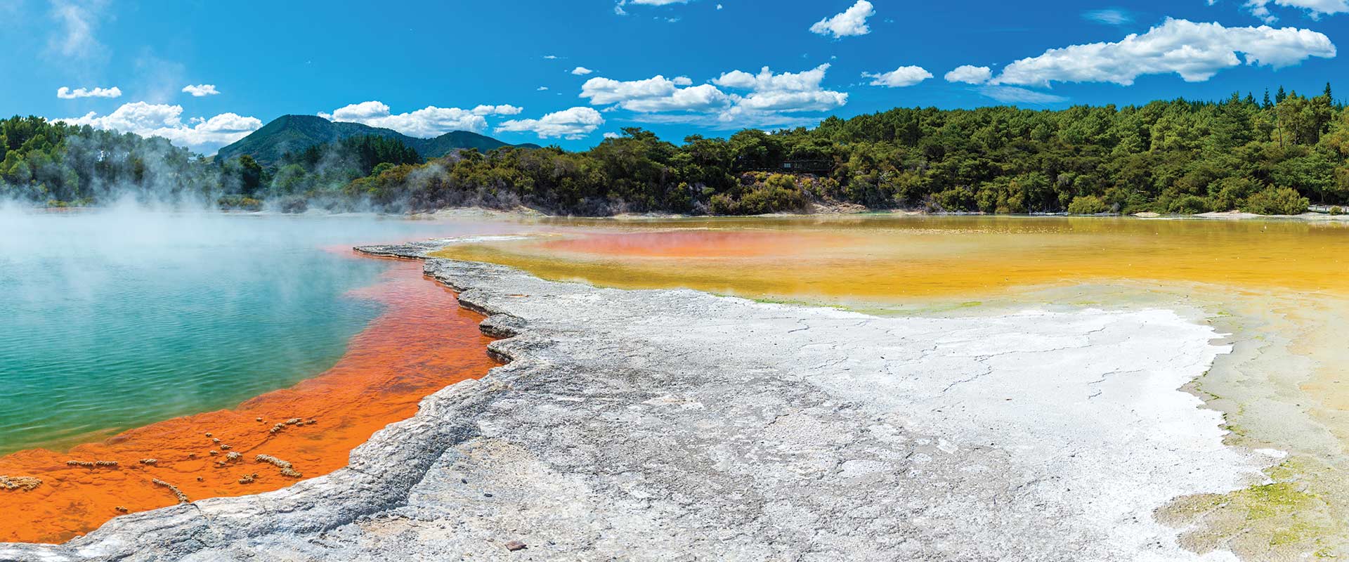 Steaming thermal pool ringed with orange sulphur bands and boiling mud pools