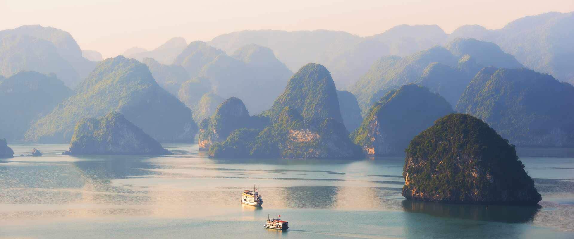 Two boats on calm water surrounded by towering limestone islands covered in dense rainforest