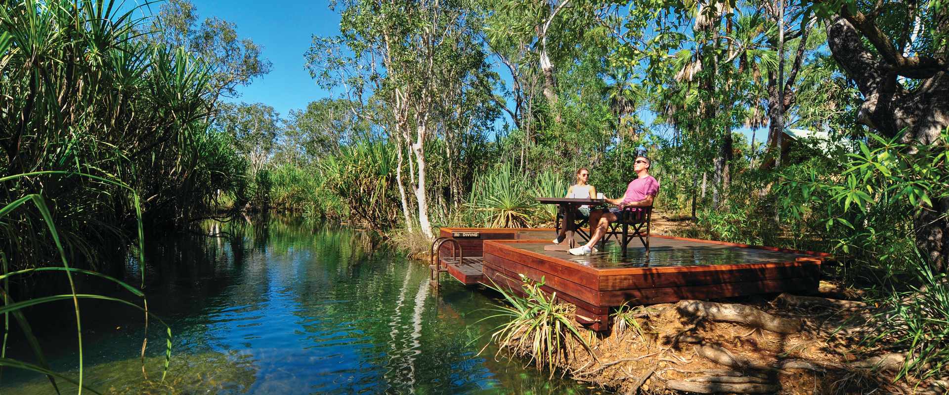 Couple sitting on deck overlooking the stream fringed with trees
