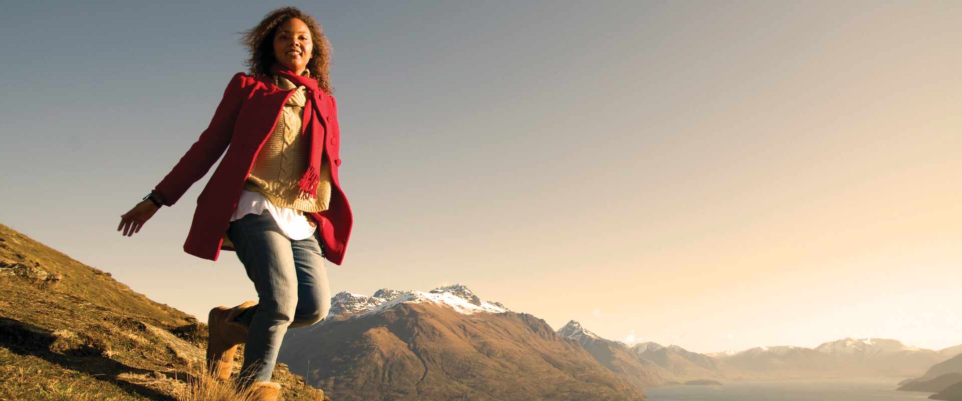 woman in red coat walking on hills with queenstown backdrop new zealand 12 5
