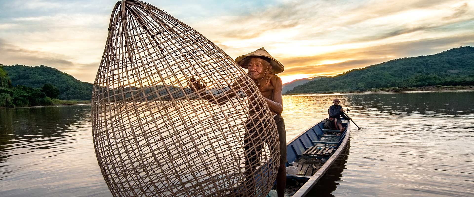 Elderly male fisherman on row boat holding a large fishing net, Cambodia