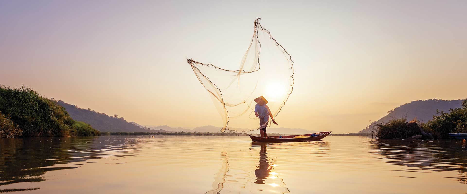 One legged rower on row boat with net flying behind, Cambodia