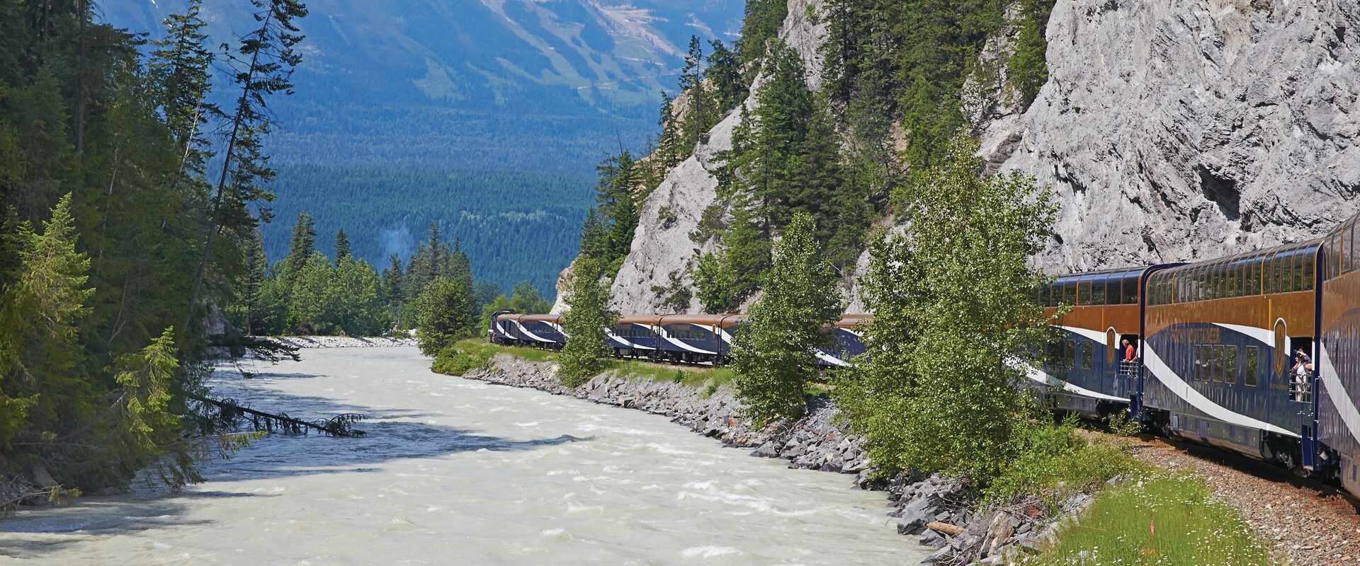 Rocky mountaineer next to a river with mountains in the background